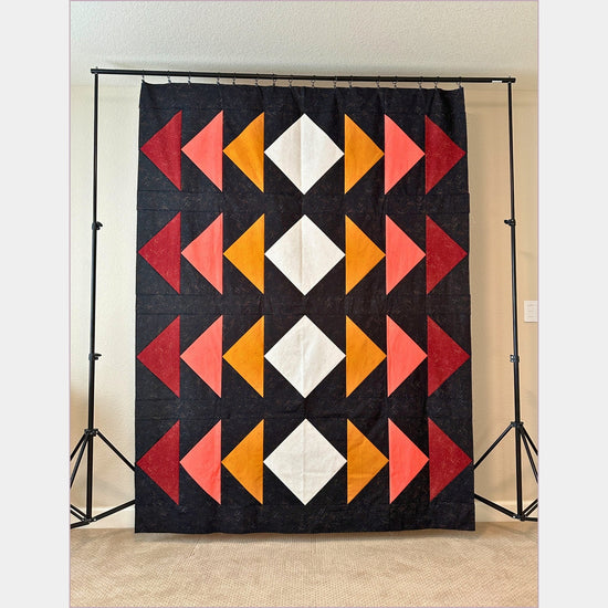 photo of a completed quilt top example created by Leslie. White diamonds in the center. Yellow, pink and red flying geese on the sides. Black background.